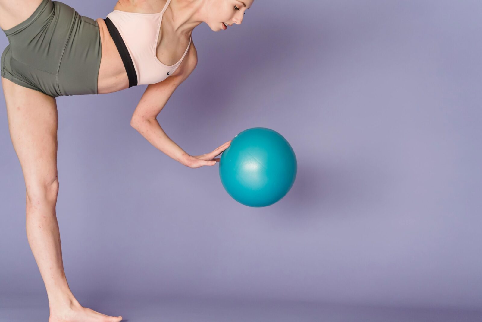 Side view of crop female in activewear doing exercises with gym ball on purple background